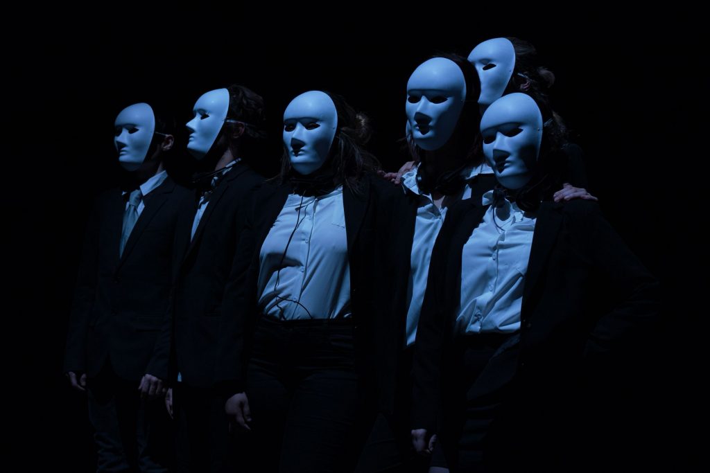 Des acteurs masqués sont sur scène, éclairés par une lumière bleue